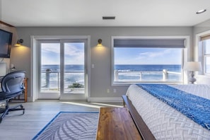 Ein Schlafzimmer mit einem Bett, einem Schreibtisch und Meerblick durch große Fenster.