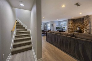 Un escalier avec des marches recouvertes de moquette et des rampes en bois, menant à un espace de vie agrémenté d’un mur en pierre et d’un grand canapé d’angle.