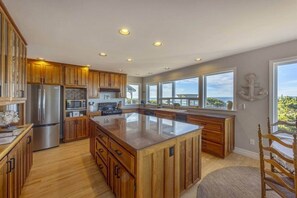 A modern kitchen with wooden cabinets, stainless steel appliances, and a large island. - Sanctuary at Seal Rock (Seal Rock)