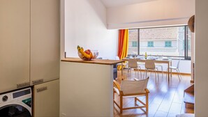Una cucina moderna con lavatrice, un'area pranzo con tavolo e sedie, e vista su un edificio attraverso una finestra.