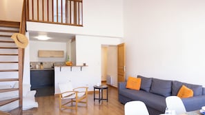 A modern living room with a grey sofa, wooden floor, and a kitchen area with a tiled backsplash. - Casa Nina – Duplex refait à neuf proche du port de Saint-Florent (Saint-Florent)