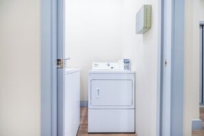 A laundry room with a front-loading washer and dryer, a utility meter, and a wall-mounted thermostat. - Esmeralda Stay | 5 min from MíA | Free parking (Miami)