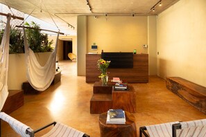 Ein Empfangsbereich mit einem Holzbüro, einer Hängematte und einer kleinen Sitzecke mit einem Buch und einer Blumenvase.