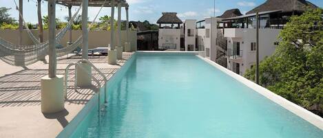 A swimming pool with a pergola and lounge chairs, surrounded by buildings with thatched roofs.