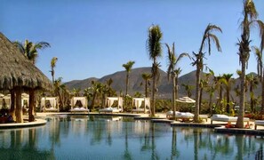 Ein Poolbereich eines Resorts mit strohgedeckten Cabanas und Palmen.