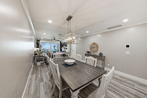 A dining area with a wooden table and chairs, a chandelier, and a view of the outdoors. - BG North 58 - 2 bed/2Bath - Pool, Tennis, Pickleball, Top Floor - Sleeps 4 (Boca Grande)