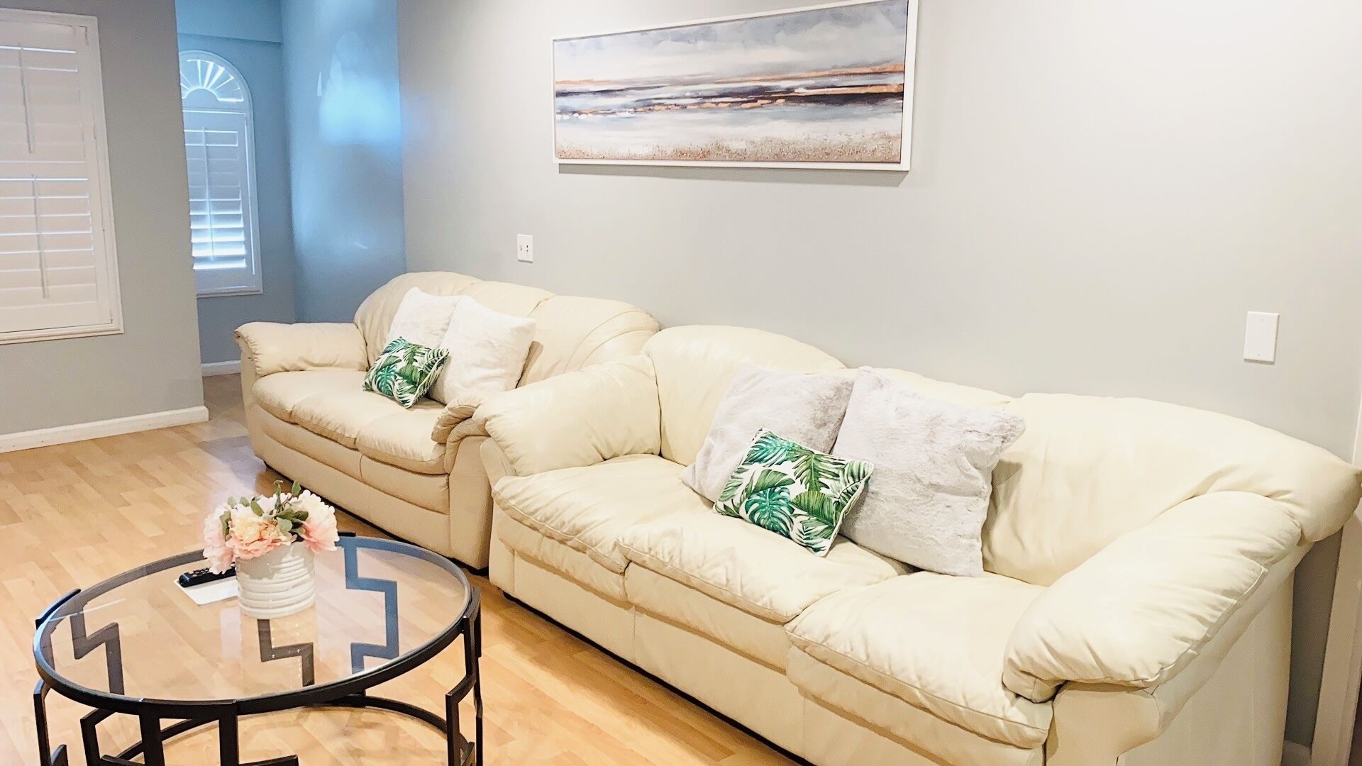 A living room with two cream-colored sofas, a glass coffee table, and a painting on the wall.