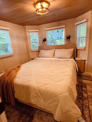A bedroom with a large bed, two bedside tables, a ceiling light fixture, and windows with blinds.