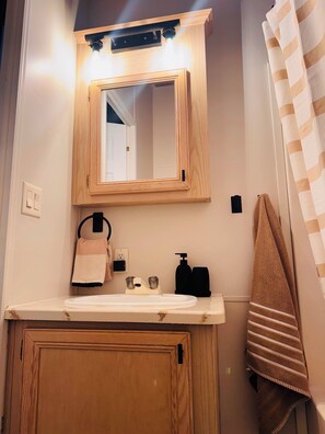 Un bagno con un mobile vanitario in legno, uno specchio, un lavabo, un porta asciugamani e una tenda da doccia.
