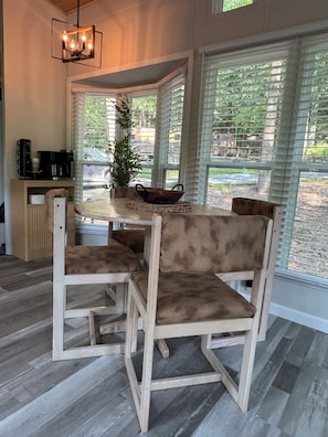 A dining area with a wooden table and chairs, a coffee machine, and a view through large windows. - Perfect Nature Getaway Awaits!
Relax, enjoy a peaceful stay surrounded by nature (Milford)
