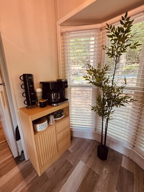 A corner with a coffee station, a plant, and a window with blinds.