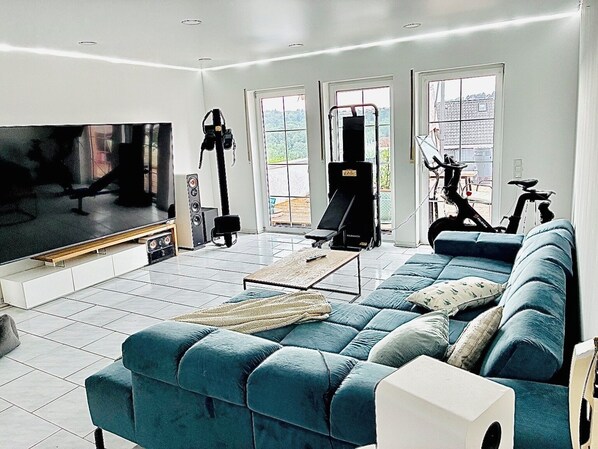 A modern living room with a large flat-screen TV, exercise equipment, a blue sofa, and a coffee table.