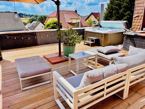 An outdoor deck with a hot tub, seating area, and a potted plant.