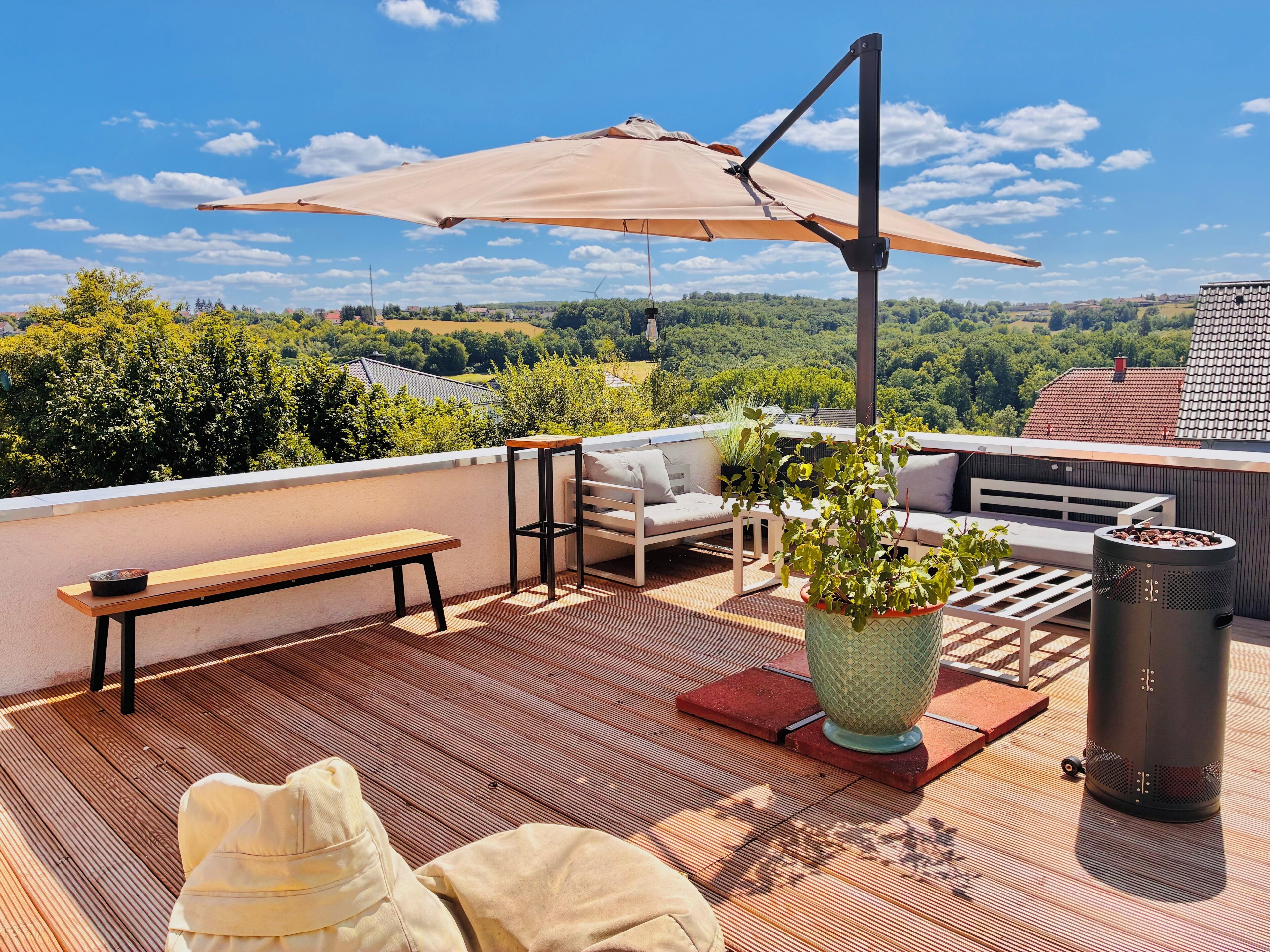 A rooftop terrace with a wooden bench, outdoor furniture, a potted plant, and a large umbrella.