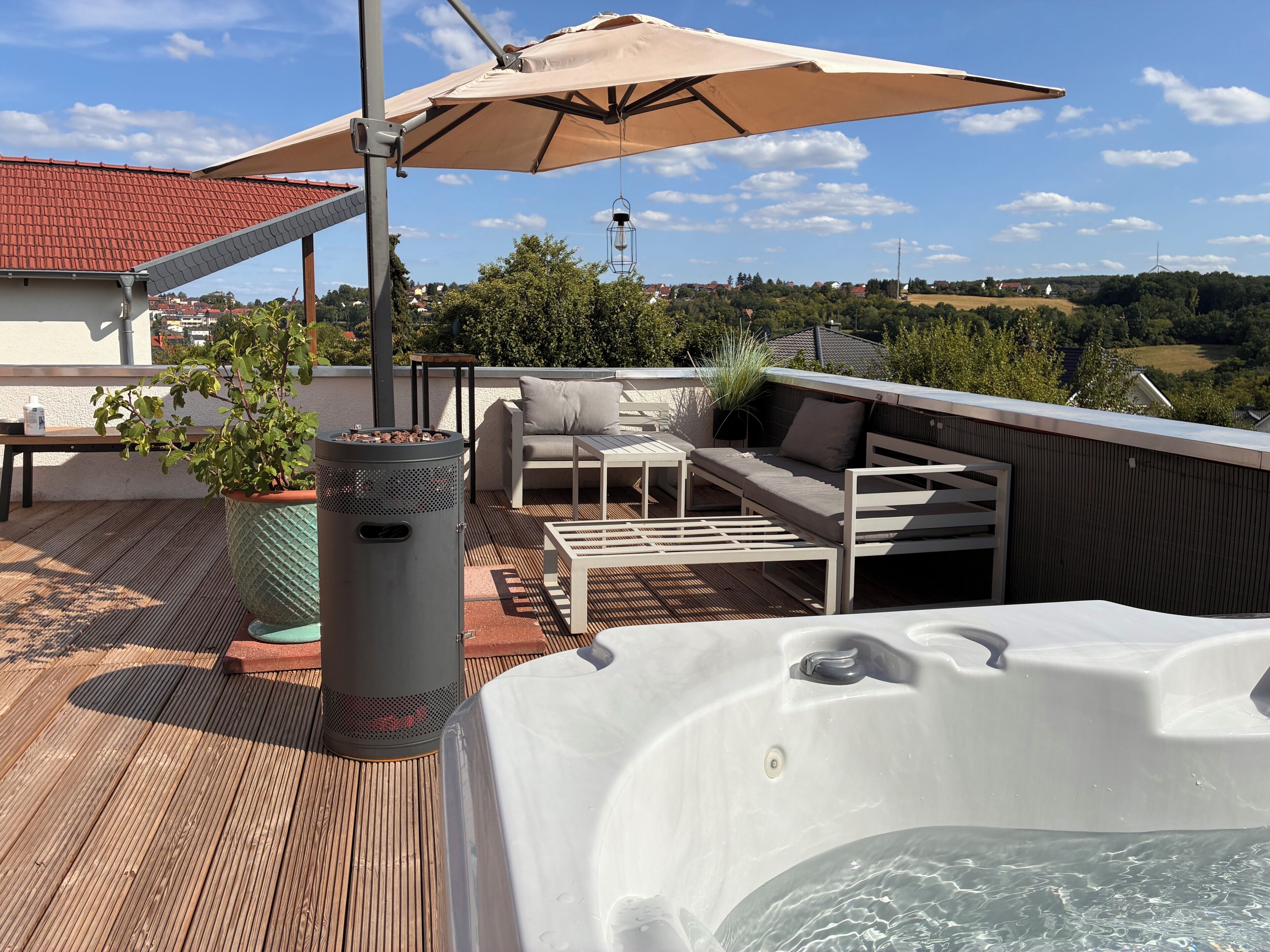 Eine Dachterrasse mit Whirlpool, Gartenmöbeln und einem großen Sonnenschirm.