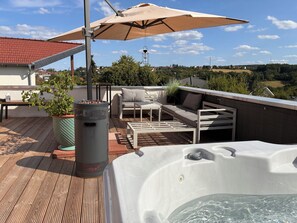 Eine Dachterrasse mit Whirlpool, Gartenmöbeln und einem großen Sonnenschirm.