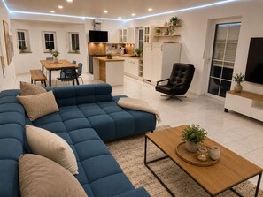 A modern living room with a sectional sofa, a dining area, and a kitchen.