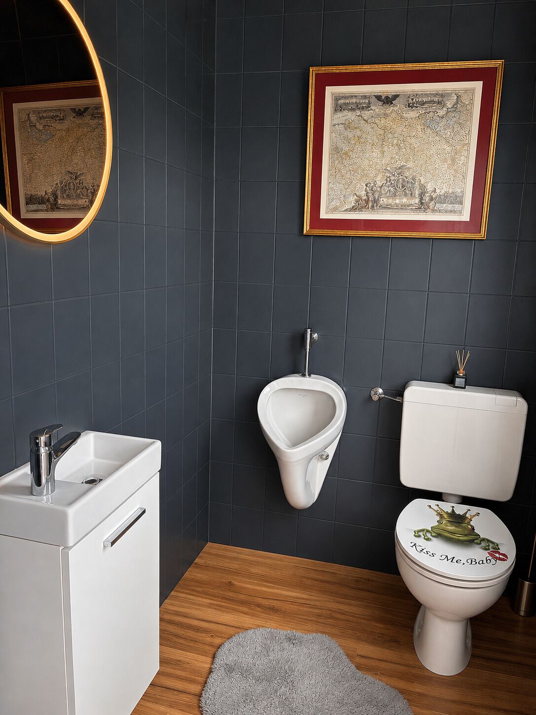 Et moderne badeværelse med et hvidt urinal, et toilet med et dekorativt låg, en vask med armatur og et indrammet kort på væggen.