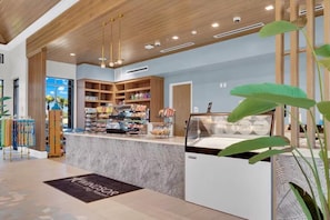 Ein modernes Interieur mit einer zentralen Theke, auf der verschiedene Speisen präsentiert werden, Holzregalen mit Produkten und einer großen Pflanze im Vordergrund.