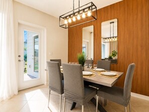 A dining area with a wooden wall, a chandelier, and a view through a glass door. - Modern 5BR Windsor Cay Retreat | Private Pool + Game Room (Clermont)