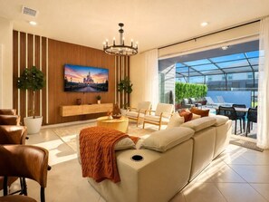 Een moderne woonkamer met een bank, stoelen, een televisie en een groot raam met uitzicht op een groen gebied.