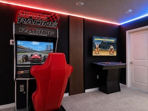 Ein rennstrecken-inspiriertes Zimmer mit Rennsimulator-Ausstattung, darunter ein roter Rennsitz und ein großer Bildschirm, der ein Rennspiel zeigt.