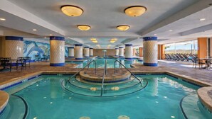 An indoor swimming pool with a central circular platform, surrounded by lounge chairs and a tiled floor. - Oceanfront Condo w/ Pools & Lazy River (North Myrtle Beach)