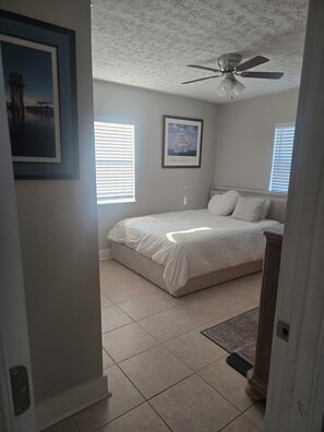 Ein Schlafzimmer mit einem Bett, einem Deckenventilator und zwei Fenstern mit Jalousien.