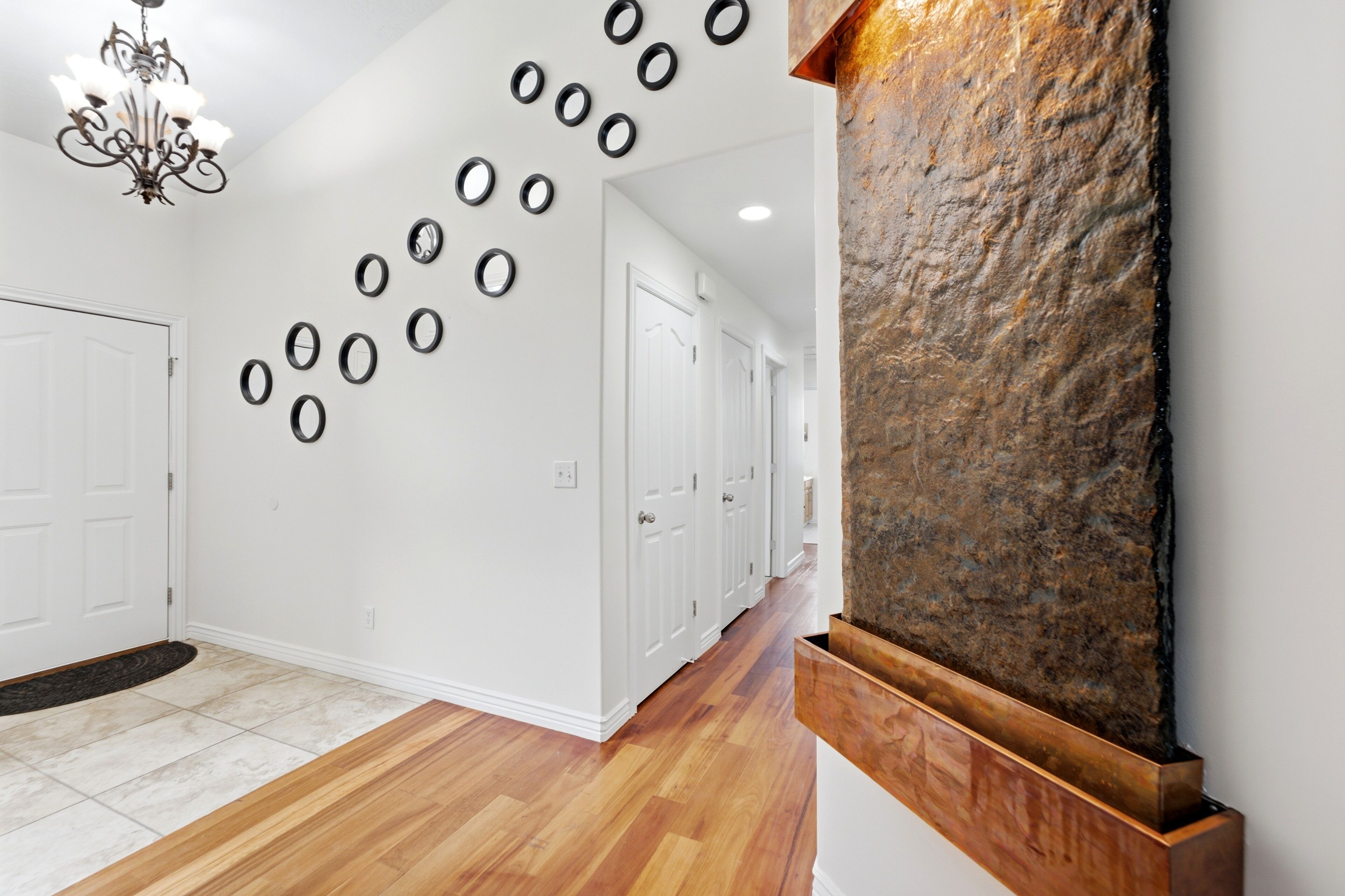 Un couloir doté d’un plancher en bois, de murs blancs et d’une série de miroirs ronds accrochés au mur. Une grande sculpture en pierre se trouve sur la droite.