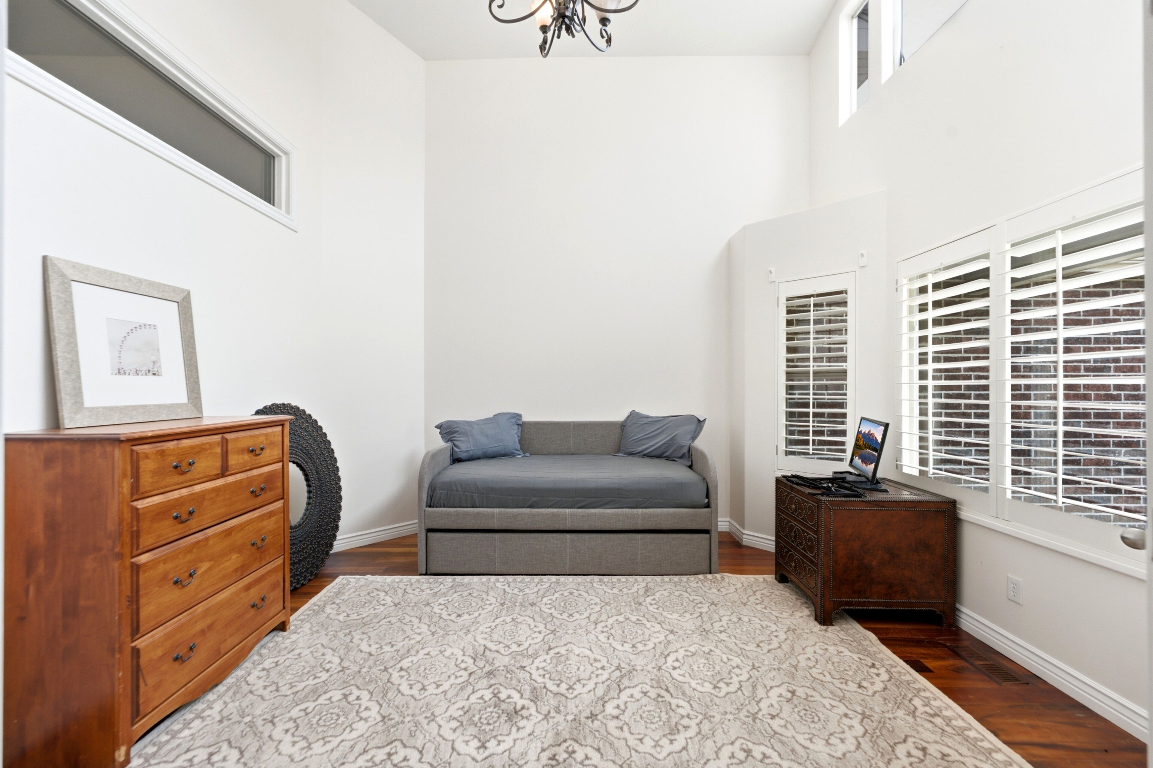 Un dormitorio con cama, cómoda, alfombra y ventana con persianas.