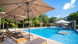 A swimming pool with lounge chairs and umbrellas, surrounded by greenery. - Apartment in Pto. Morelos Rooftop (Puerto Morelos)
