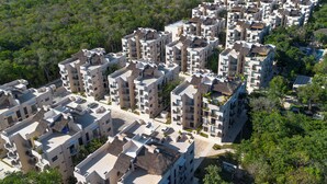 A high-rise residential building with multiple balconies, a swimming pool, and a lush green landscape surrounding the property. - Apartment in Pto. Morelos Rooftop (Puerto Morelos)