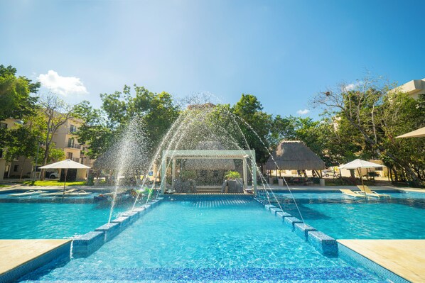 A swimming pool with a water feature in the center, surrounded by lounge chairs and umbrellas.