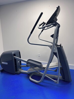 Un vélo d’appartement, doté d’un écran numérique, est placé sur un sol bleu, devant un mur blanc.