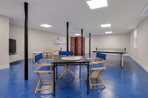 Une pièce comprenant une table de ping-pong, une table ronde avec des chaises, un téléviseur et un élément décoratif mural.