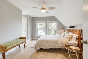 Ein Schlafzimmer mit Bett, einer Sitzbank, einem Schreibtisch, einem Deckenventilator und großen Fenstern.