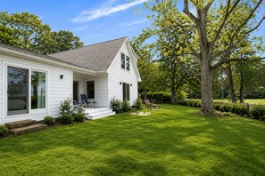 Une maison blanche avec un porche abrité, une pelouse et un grand arbre.