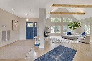 Uma sala de estar ampla com um sofá seccional grande, um tapete azul e um vigamento de madeira no teto.