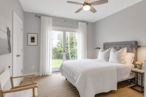 A bedroom with a bed, a nightstand, a chair, a ceiling fan, and a view of the outdoors. - Waterfront 3 Bedroom Marina Retreat • East Hampton • HeatedPool (East Hampton)