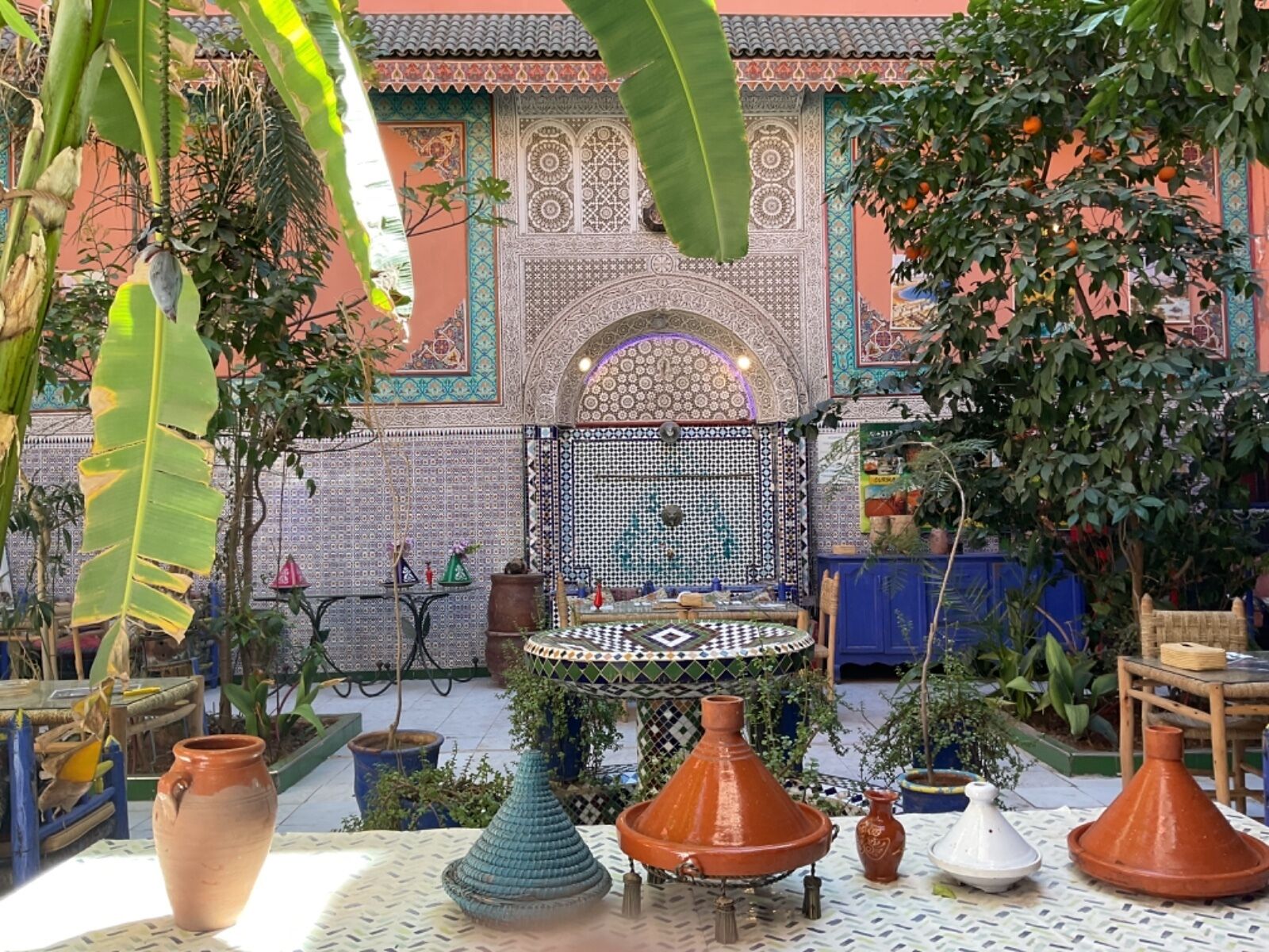 Un patio con una fuente, plantas en macetas y baldosas tradicionales marroquíes.