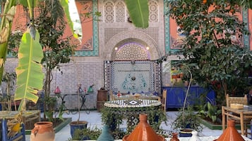 Un patio con una fuente, plantas en macetas y baldosas tradicionales marroquíes.