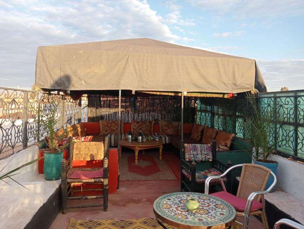 Un área de estar al aire libre con un gran toldo, mobiliario de mimbre y una mesa con motivos decorativos.