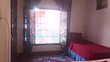 Un dormitorio con cama, una ventana con cortinas, un tapete estampado y una lámpara fijada a la pared.