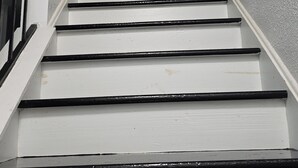 Una escalera con escalones blancos y barandillas negras, que conduce a un rellano con una lámpara.