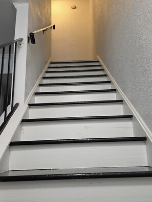 A staircase with white steps and black handrails, leading to a landing with a light fixture.