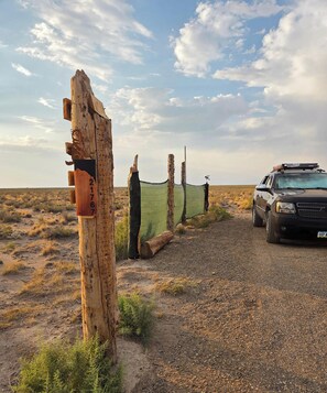 A vehicle parked on a gravel path with a wooden post and a green netting structure in the background.