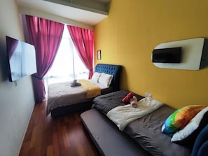 A room with two beds, a flat-screen TV mounted on the wall, and a window with red curtains.