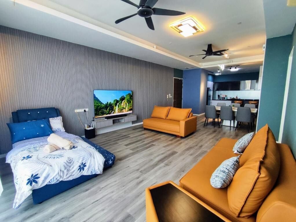 A modern hotel room with a bed, sofa, TV, and kitchenette.