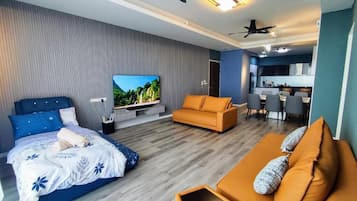 A modern hotel room with a bed, sofa, TV, and kitchenette.