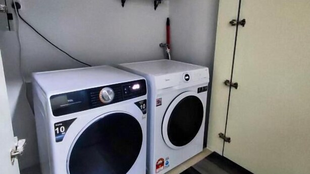 A laundry room with two washing machines, a shelf with toiletries, and a wooden floor.